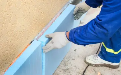 Ręce w rękawiczkach układają niebieski styropian na fundamencie. To kluczowy etap budowy, by wybrać odpowiedni styropian na fundament.