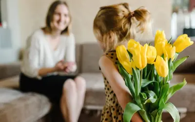 Mała dziewczynka z bukietem żółtych tulipanów za plecami, przygotowuje życzenia urodzinowe dla cioci.