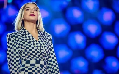 Młoda, amerykańska piosenkarka country w stylowej, szachownicowej marynarce na tle niebieskich świateł.