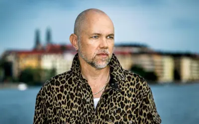 Peter LeMarc i leopardmönstrad jacka, redo för en konsert. Bakgrunden visar en stad vid vattnet.
