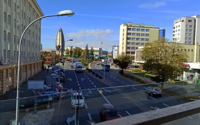 Widok na ruchliwą ulicę w Rzeszowie, z charakterystycznym budynkiem przypominającym żagiel w tle. W oddali widać **ogrody bernardyńskie rzeszów**.