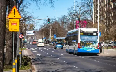 Korytarz miejski z ruchem ulicznym, autobusem i samochodami. Znaki drogowe ostrzegają przed wyjazdem.