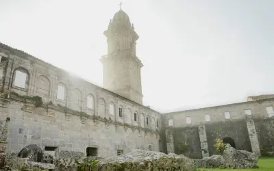 El imponente **monasterio de Oia** se alza bajo un cielo brumoso, con su torre campanario y sus muros de piedra evocando historias de siglos pasados.