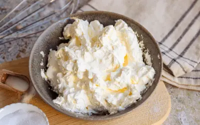 Schüssel mit luftiger, weißer italienischer Buttercreme, bereit für süße Kreationen. Daneben Zucker und ein Schneebesen.