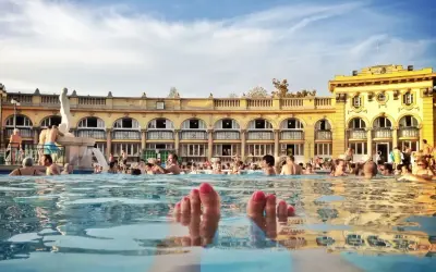 Fötter sticker upp ur vattnet i ett soligt budapest spa. Människor badar och njuter av den vackra arkitekturen.