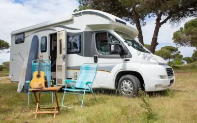 En vit husbil, en personbil klass 2, står parkerad i gräset. Surfbrädor, en gitarr och campingstolar antyder en avkopplande semester.