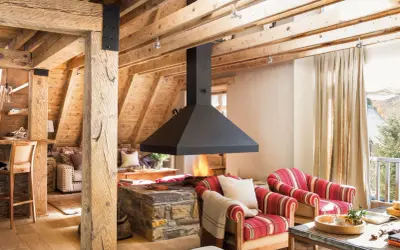 Chimenea central de diseño moderno, uno de los tipos de chimeneas que aporta calidez a este salón rústico con vigas de madera.