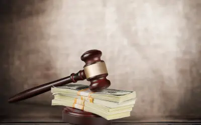 Młotek sędziowski na stosie banknotów dolarowych symbolizuje sprawiedliwość i finansową kompensatę.