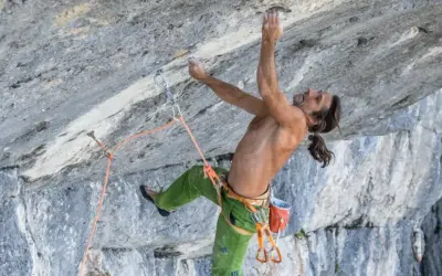 Alexander Huber klettert an einer steilen Felswand, sein Körper angespannt, die Hände greifen nach kleinen Vorsprüngen.