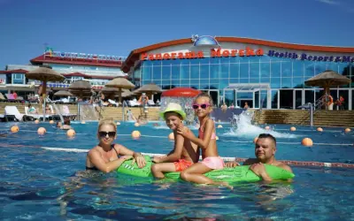 Rodzina pływa w basenie przy hotelu "Panorama Morska" z widokiem na budynek.