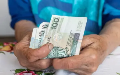 Dłonie trzymają banknoty 100 zł. Zastanawiasz się, ile wynosi najniższa emerytura z ZUS?