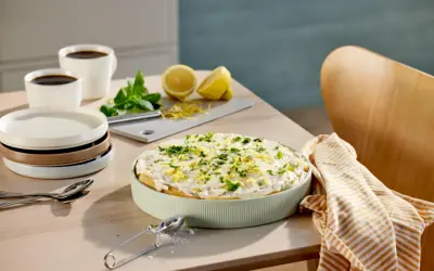 En krämig tiramisu limoncello, garnerad med citronzest och persilja, står på ett bord med kaffe och citroner.