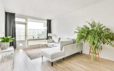 Soggiorno in casa stile nordico con divano grigio, tappeto a righe, piante verdi e grandi finestre.