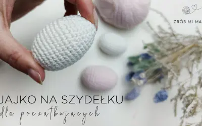 Ręcznie robione, białe jajko na szydełku, idealne na początek przygody z szydełkowaniem. W tle pastelowe włóczki i suszone kwiaty.