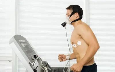 Mężczyzna w masce tlenowej i elektrodach EKG biegnie na bieżni podczas testu coopera.