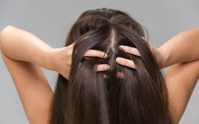 Une femme se touche les cheveux, montrant comment hydrater son cuir chevelu pour des cheveux sains et brillants.