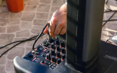Ręka podłącza kabel do miksera, pokazując, jak podłączyć przedwzmacniacz do wzmacniacza.