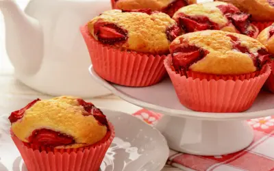 Pyszne muffiny z truskawkami w różowych papilotkach, gotowe do podania z białą czajniczkiem w tle.