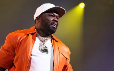 50 Cent w pomarańczowej kurtce i białej czapce, z błyszczącym naszyjnikiem, występuje na scenie. Polska publiczność szaleje!