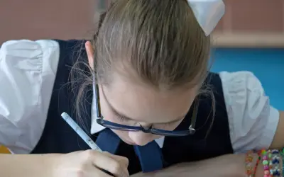 Dziewczynka w okularach ćwiczy grafomotorykę, pisząc długopisem.