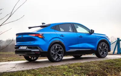 Niebieski Renault Rafale z dynamiczną linią dachu, zaparkowany na mokrej drodze.