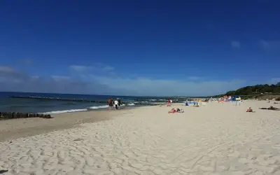 Słoneczna plaża wschodnia Ustka z ludźmi spacerującymi i odpoczywającymi na piasku.