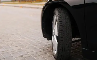 Błyszczące, czarne auto na kostce brukowej. Widoczna opona zimowa, której wiek można ocenić po bieżniku.