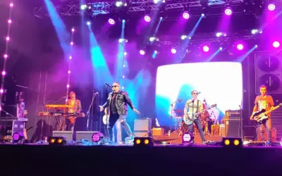 Zespół gra na scenie podczas koncertów w Stalowej Woli. Wokalista w skórzanej kurtce, gitarzyści i klawiszowiec.