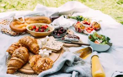 Pyszne jedzenie na piknik: świeże croissanty, bagietka, truskawki, wiśnie, sałatka, kiełbasa i napoje.