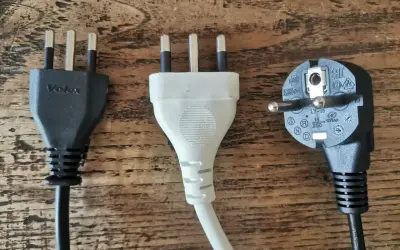 Trzy wtyczki elektryczne, w tym dwie z trzema bolcami, typowe dla gniazdek we Włoszech, leżą na drewnianym blacie.