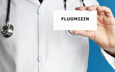 Lekarz w białym kitlu trzyma kartkę z napisem FLUOMIZIN. Stetoskop wisi na jego szyi.