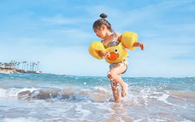 Radosna dziewczynka w żółtym kaczuszce bawi się na plaży. Idealna turcja pogoda maj na wakacje.