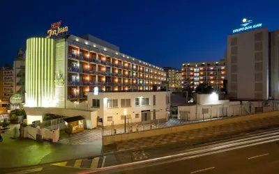 Hotel Don Juan Resort nocą, z neonowym oświetleniem i widokiem na wiele balkonów.