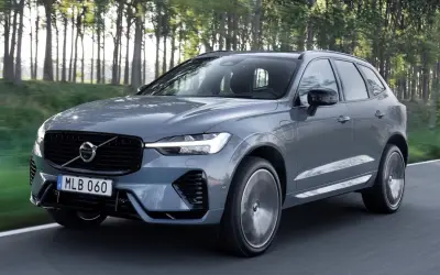Szary Volvo XC60 z napędem hybrydowym, poruszający się po leśnej drodze. Dostępne różne silniki.