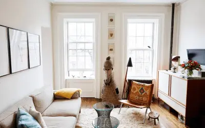 A bright living room with a sofa, fluffy rug, and two windows, demonstrating how to make a small space feel large with light and airy decor.