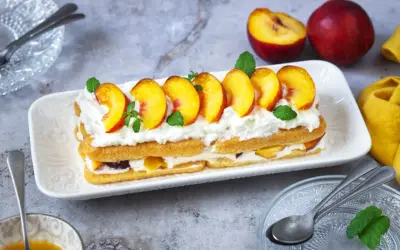 Delizioso tiramisù alle pesche, con strati di savoiardi, crema soffice e pesche fresche, guarnito con menta.