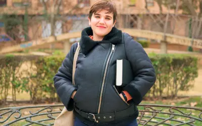 Uśmiechnięta osoba w czarnej, ocieplanej kurtce przejściowej duże rozmiary, trzymająca książkę.