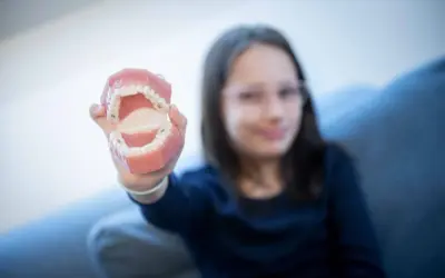 Dziewczynka trzyma model szczęki, pokazując zęby. Może to być związane z edukacją o higienie jamy ustnej, gdzie azotan potasu zastosowanie ma w pastach do zębów.