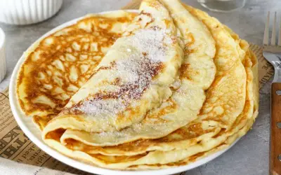 Ein Stapel goldbrauner Pfannkuchen, bestreut mit Zucker. Ein einfaches Pfannkuchen Rezept für jeden Tag.