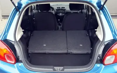 Błękitny Mitsubishi Space Star z otwartym bagażnikiem. Widoczne złożone tylne siedzenia, tworzące płaską przestrzeń ładunkową.