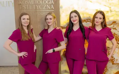 Cztery kobiety w uniformach medycznych stoją obok siebie przed tablicą z napisem "Kosmetologia Estetyczna".