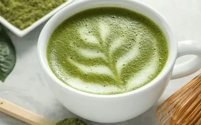 Un délicieux café matcha latte, orné d'une mousse crémeuse et d'une pincée de poudre de matcha sur une cuillère en bois.