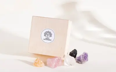 Drewniane pudełko z naklejką "BASIC CRYSTALBOX" i pięcioma surowymi kamieniami: bursztynowym, różowym kwarcem, kryształem górskim, czarnym turmalinem i ametystem. Każdy cenny kamień emanuje naturalnym blaskiem.