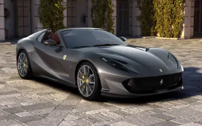 Szary kabriolet Ferrari 812 GTS z żółtymi zaciskami hamulcowymi stoi na brukowanym dziedzińcu przed budynkiem porośniętym bluszczem.