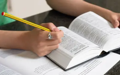 Mani che studiano un dizionario, scrivendo con una matita. Scoprire parole italiane affascinanti è un viaggio.