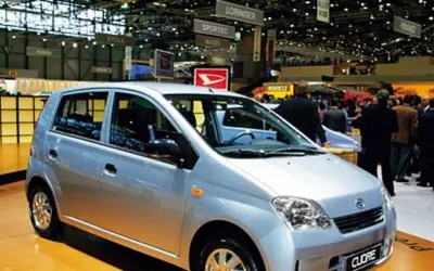 Srebrny Daihatsu Cuore na targach motoryzacyjnych, wśród tłumu ludzi i innych stoisk.