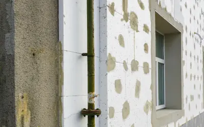 Budynek w trakcie termoizolacji styropianem. Zastanawiasz się, ile kosztuje termoizolacja budynku? Widoczna rura i okno.
