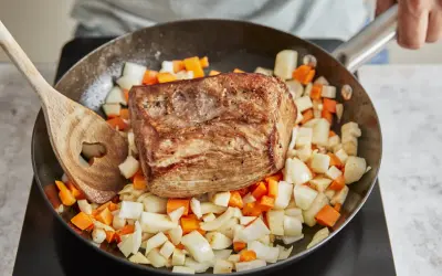 Ein gebratener Rinderbraten ruht auf gewürfeltem Wurzelgemüse in einer Pfanne. Perfekt für ein herzhaftes rinderbraten rezept.