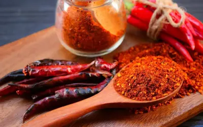 Ein Holzlöffel voller Cayennepfeffer-Flocken zeigt, woraus Cayennepfeffer hergestellt wird: getrocknete Chilischoten.
