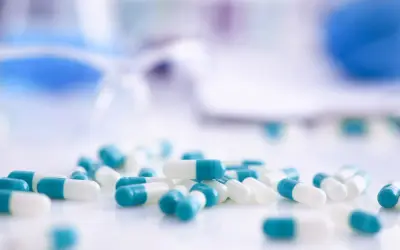 Kapsułki z antybiotykami w kolorze białym i turkusowym leżą na białej powierzchni.
